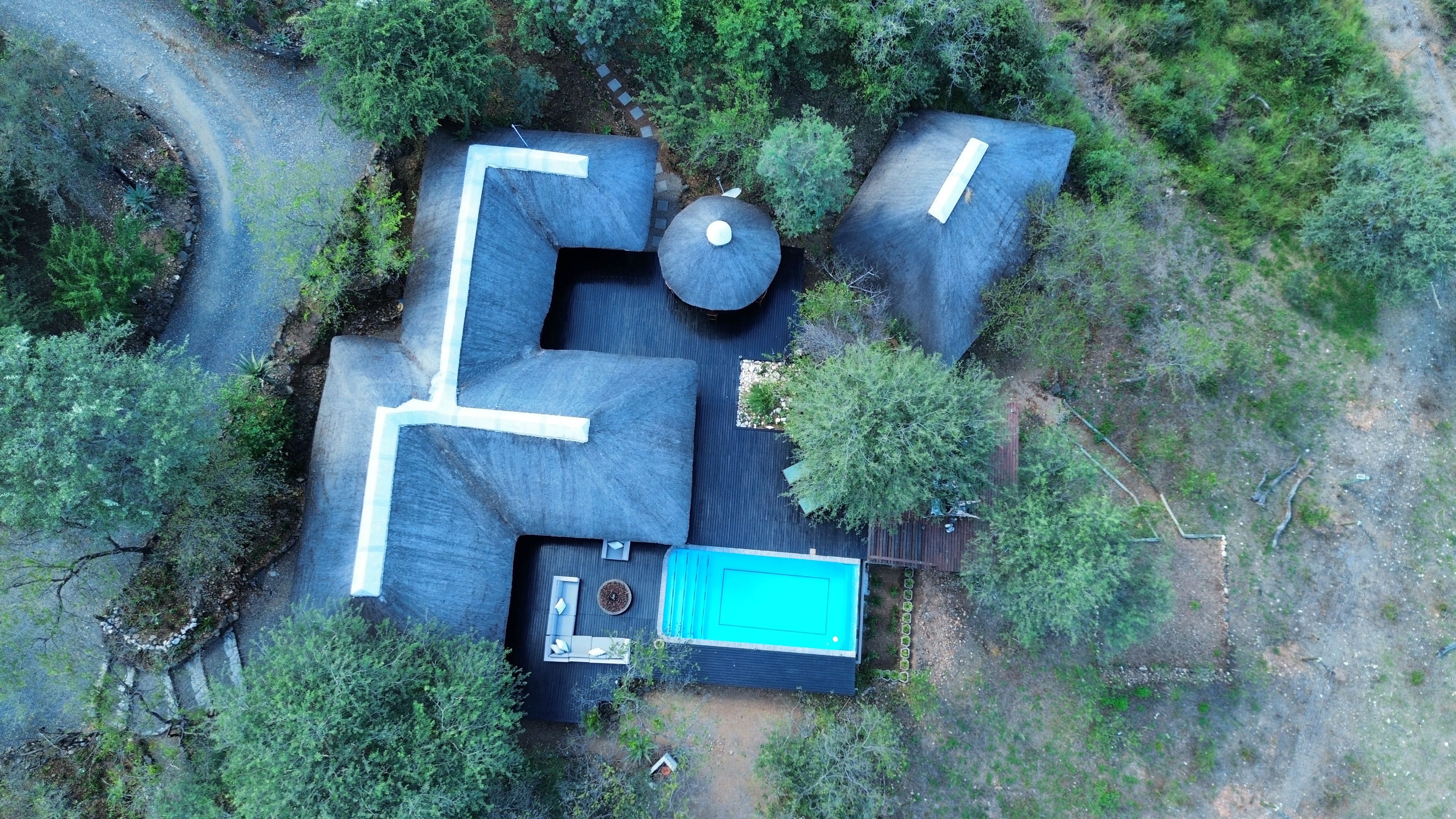 Vue aérienne d’une propriété comprenant un grand bâtiment à la forme irrégulière, une piscine et une végétation luxuriante.