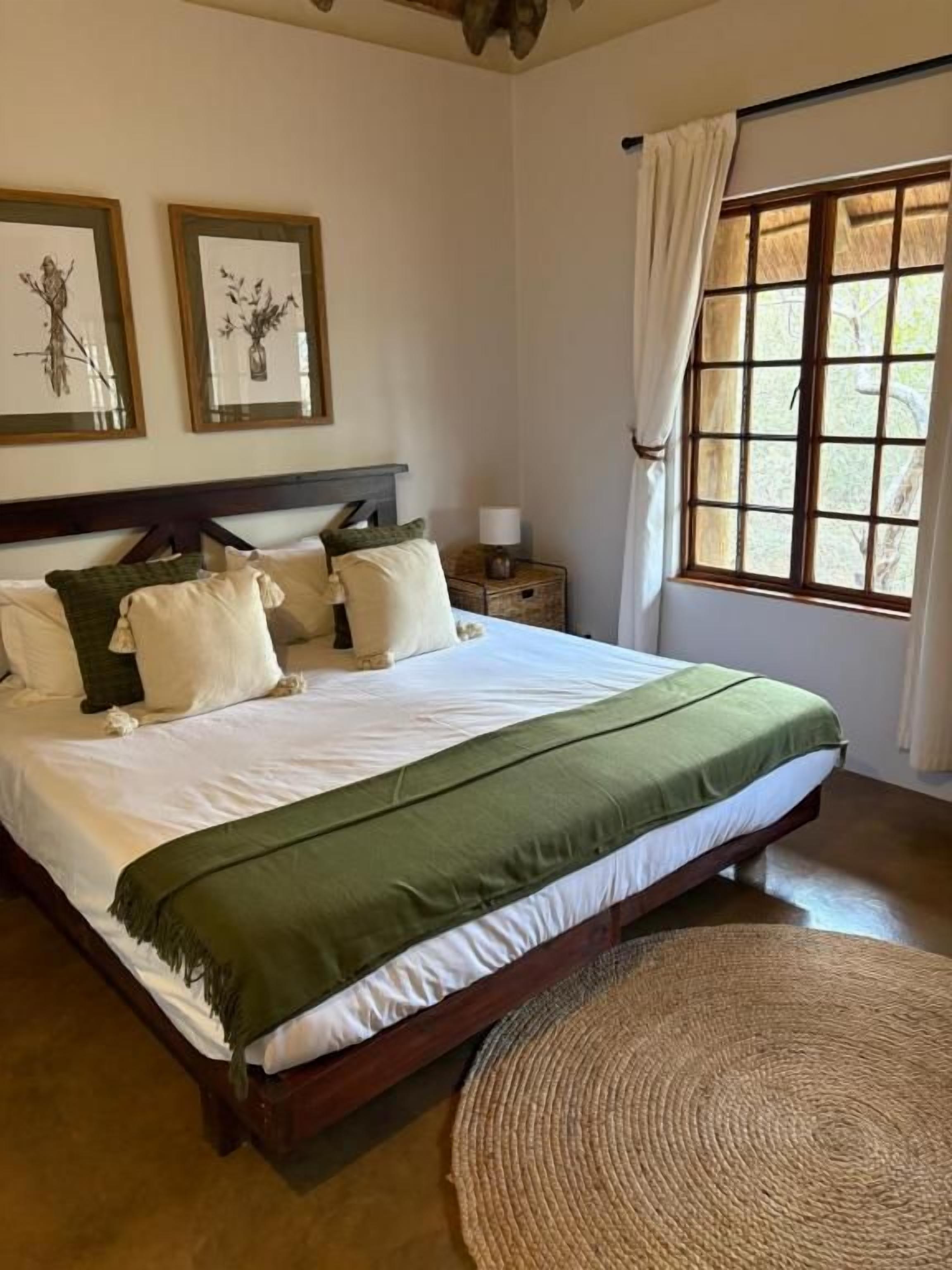 A bedroom with a large bed, a nightstand with a lamp, and a window with curtains.