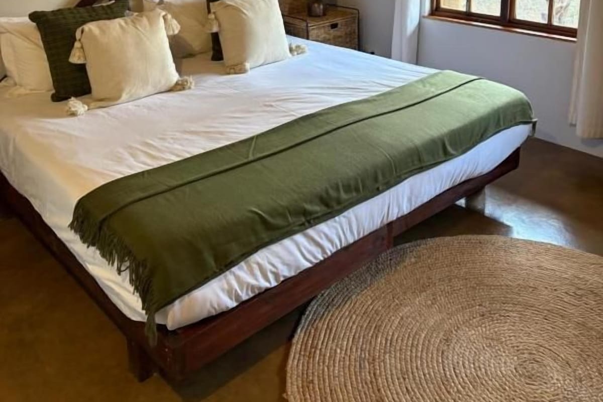 Une chambre à coucher avec un grand lit, une table de chevet avec une lampe et une fenêtre avec des rideaux.