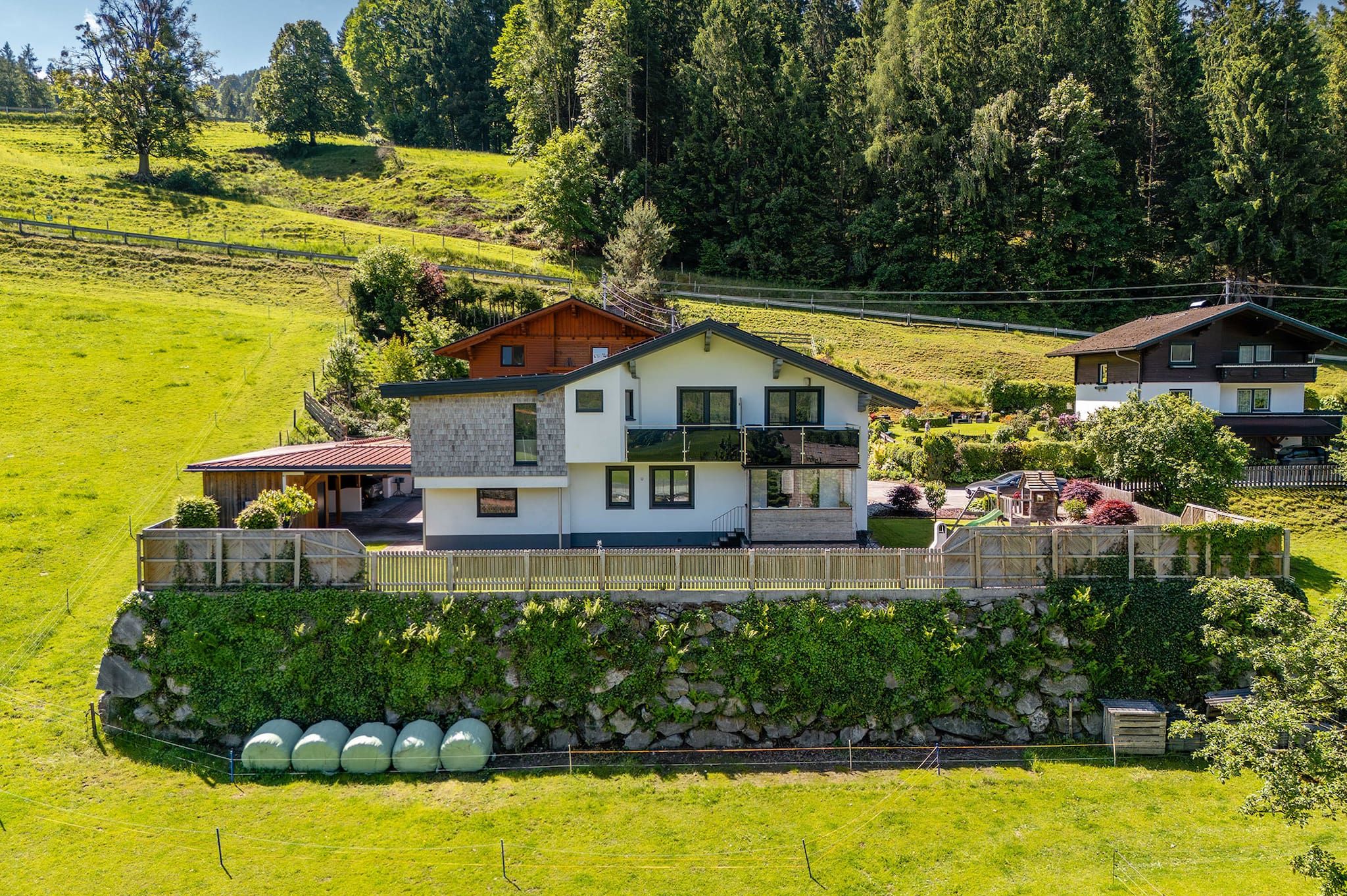 A two-story house with a stone foundation, a balcony, and a fenced garden area.