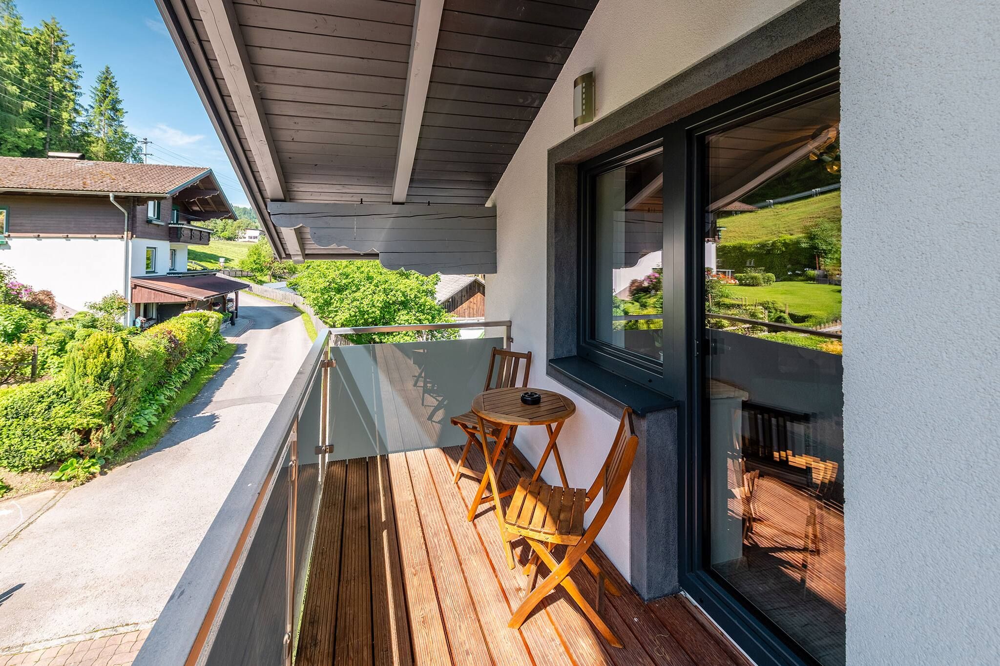 Ein Balkon mit Holztisch und Stühlen, einer Glastür und Blick auf eine grüne Landschaft.