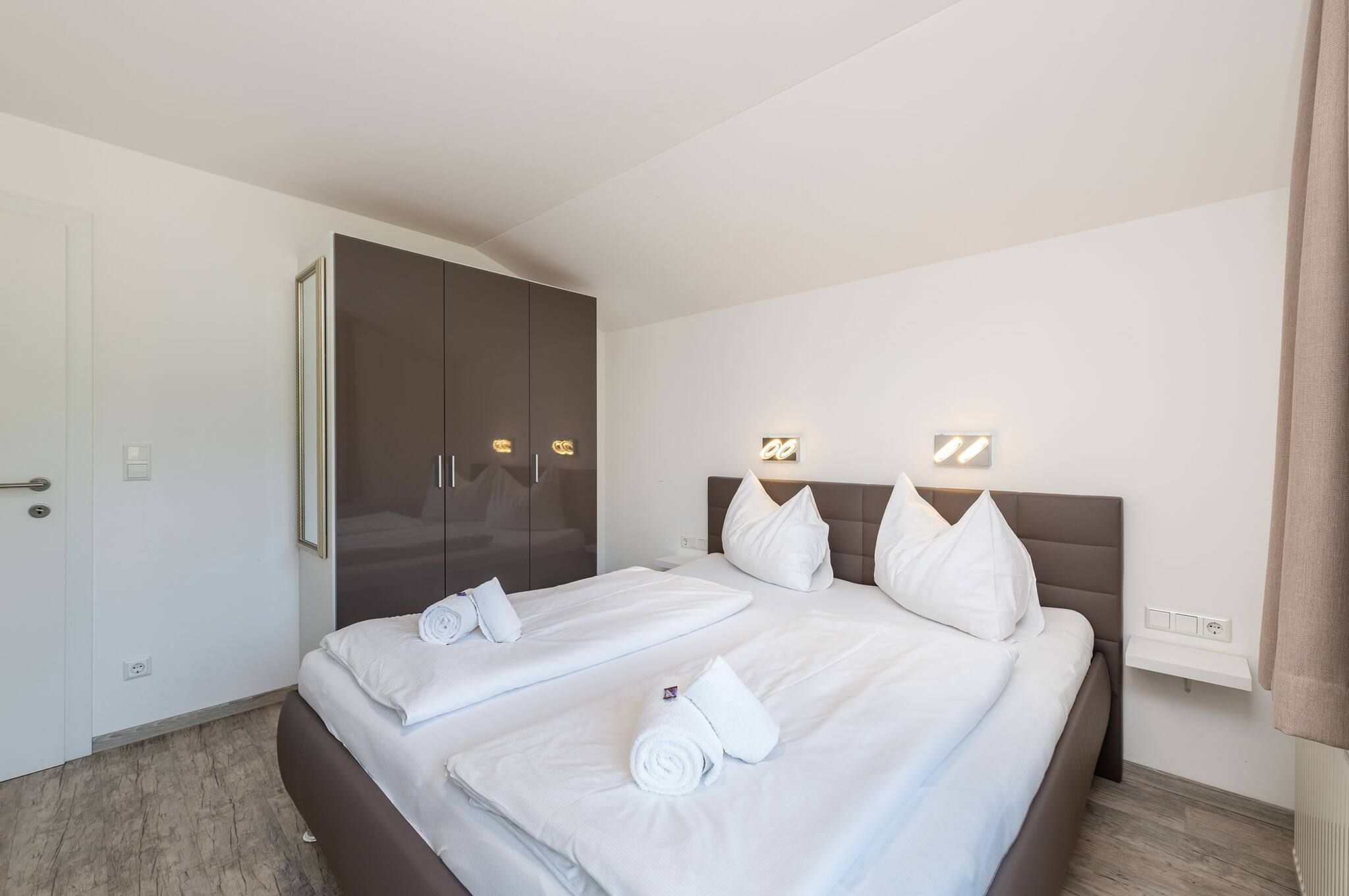 A hotel room with a bed, a wardrobe, and a bedside table.