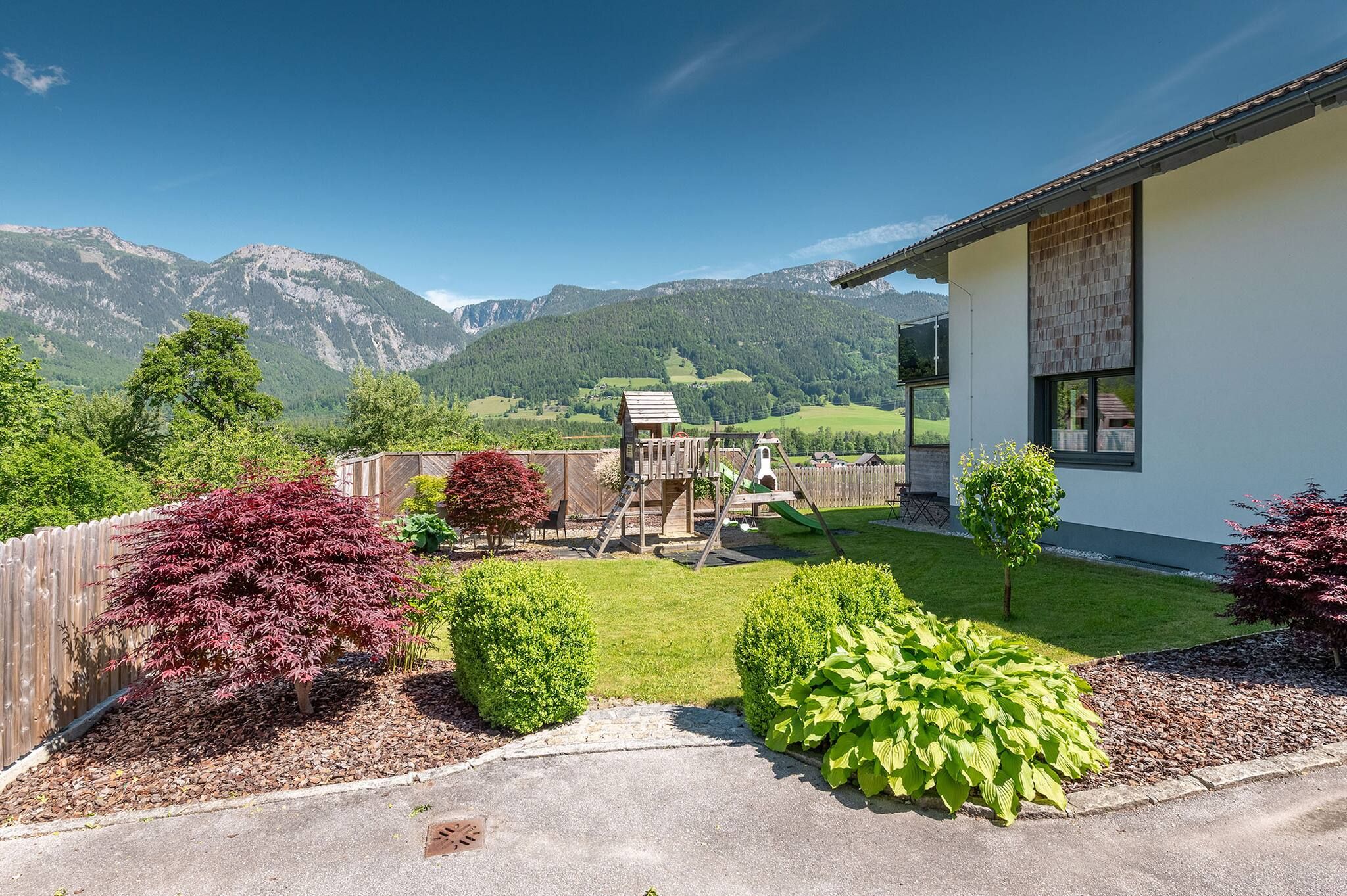 A residential property with a play area, a white building with a window, and a mountainous landscape in the background.