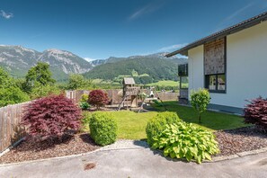 A residential property with a play area, a white building with a window, and a mountainous landscape in the background.