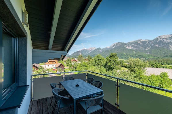 A balcony with a table and chairs, overlooking a mountainous landscape with houses in the distance.
