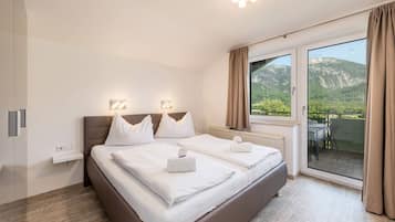 A modern bedroom with a large bed, a view of mountains through the window, and a balcony.