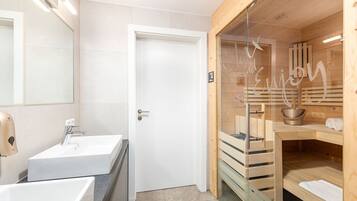 A modern bathroom with a white sink, a mirror, and a glass-enclosed sauna area.
