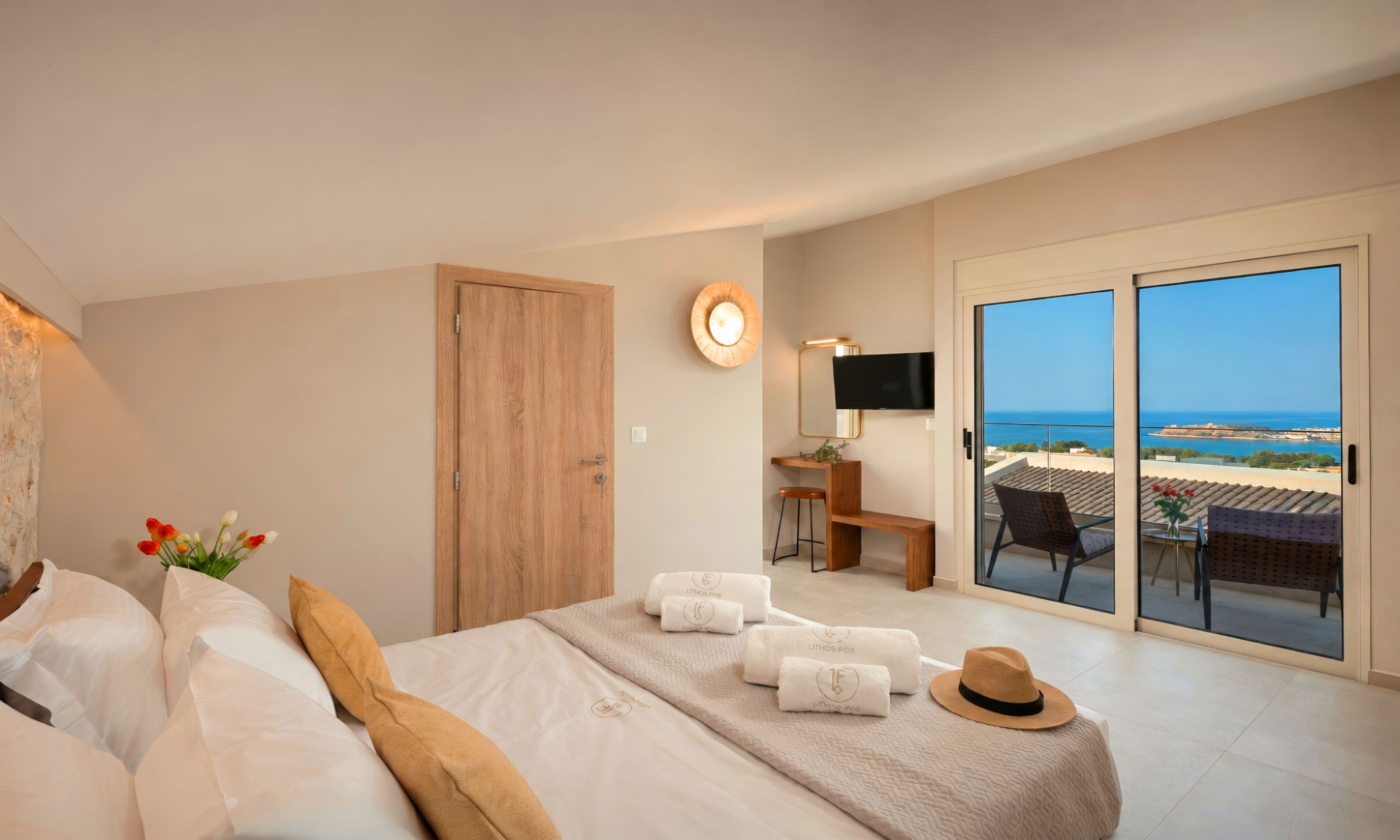 Quarto de hotel com cama, TV, escrivaninha e varanda vista para o mar.
