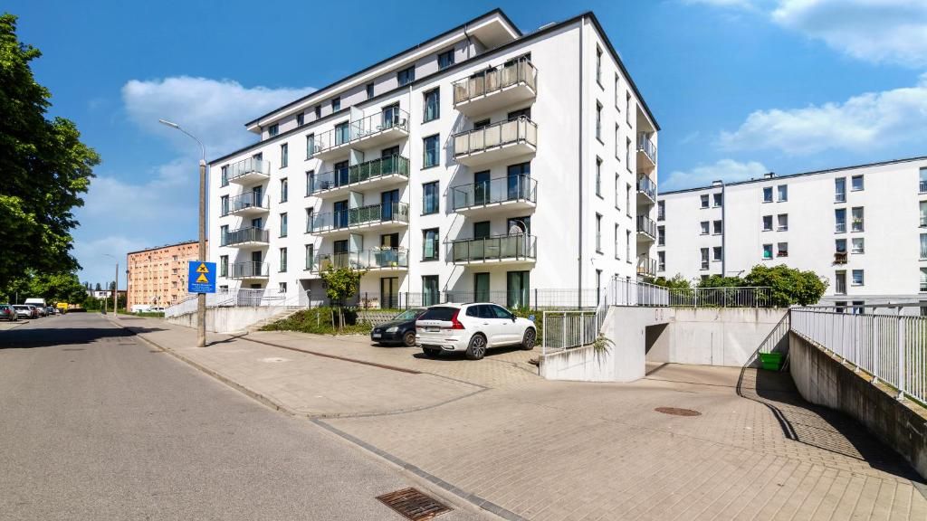 Un edifici residencial de diverses plantes amb balcons, una zona d'aparcament i un cel serè.