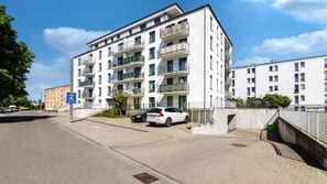 Edifício residencial com vários andares, varandas, área de estacionamento e céu claro.