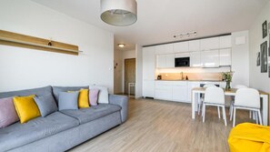 Uma sala de estar moderna com um sofá cinza, uma mesa de jantar com cadeiras e uma cozinha com armários brancos e um micro-ondas.