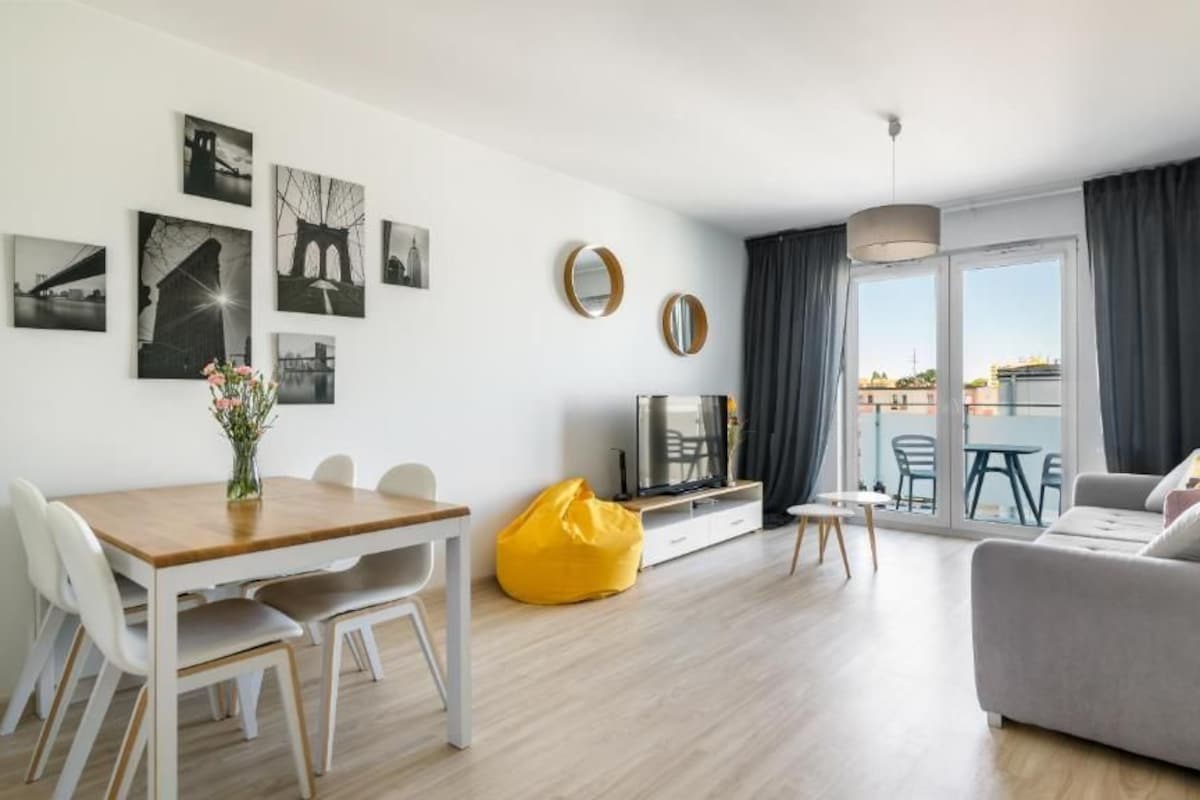 Una sala de estar moderna con un sofá, una mesa de comedor con sillas, un televisor y obras de arte en las paredes.