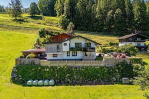 Ein zweistöckiges Haus mit einer Steinschmalseite, einer Holzterrasse und einem Garten mit verschiedenen Pflanzen.