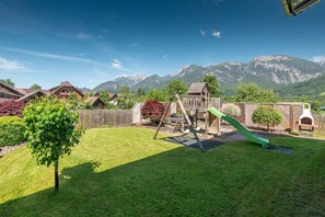 A backyard with a wooden playset, a green slide, and a tree.
