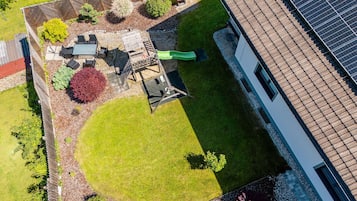 An aerial view of a residential property with a fenced garden, outdoor seating area, and a solar panel array.