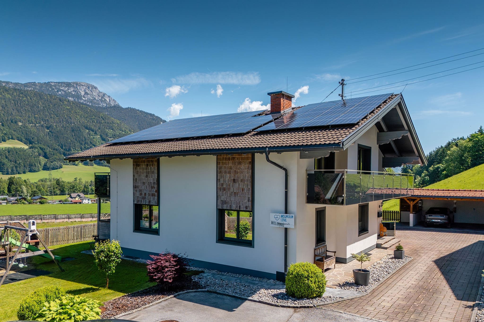 Ein zweistöckiges Gebäude mit geneigtem Dach, Solaranlagen und einem Schild, auf dem 'Mountain Love Welcome' steht.