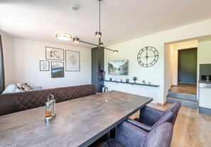 A modern kitchen with a built-in oven, a dining area with a long table and cushioned seating, and a wall-mounted clock.
