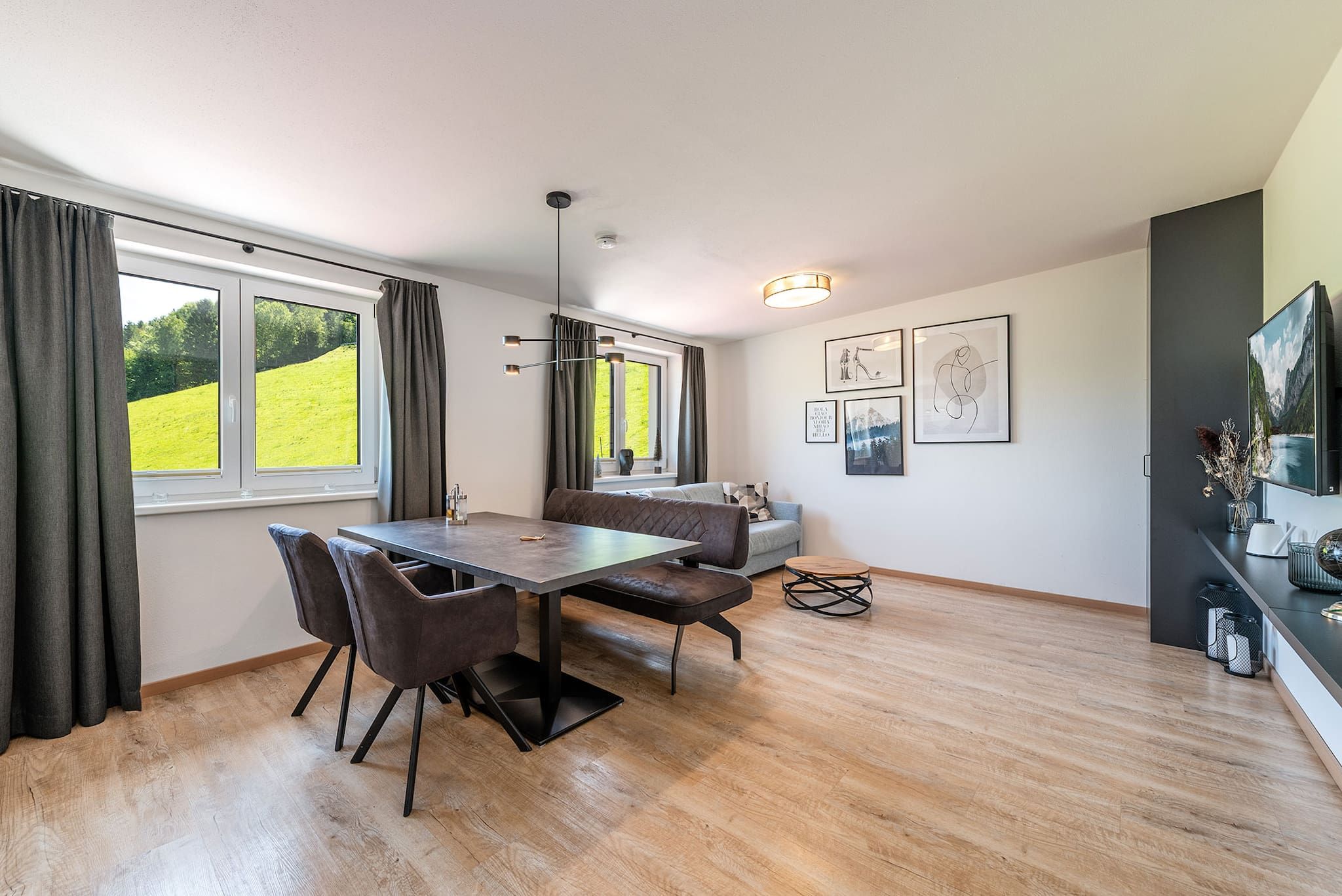 A modern dining area with a wooden table and chairs, a sofa, and a television on a stand.