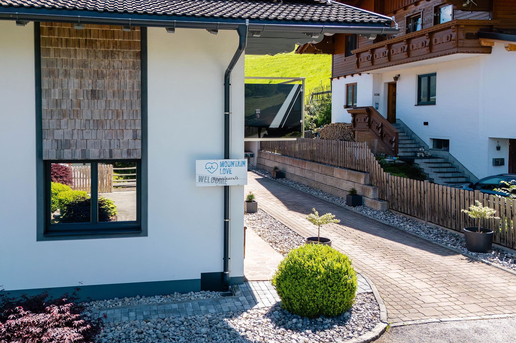 A mountain lodge with a welcoming sign, a wooden fence, and a paved driveway.