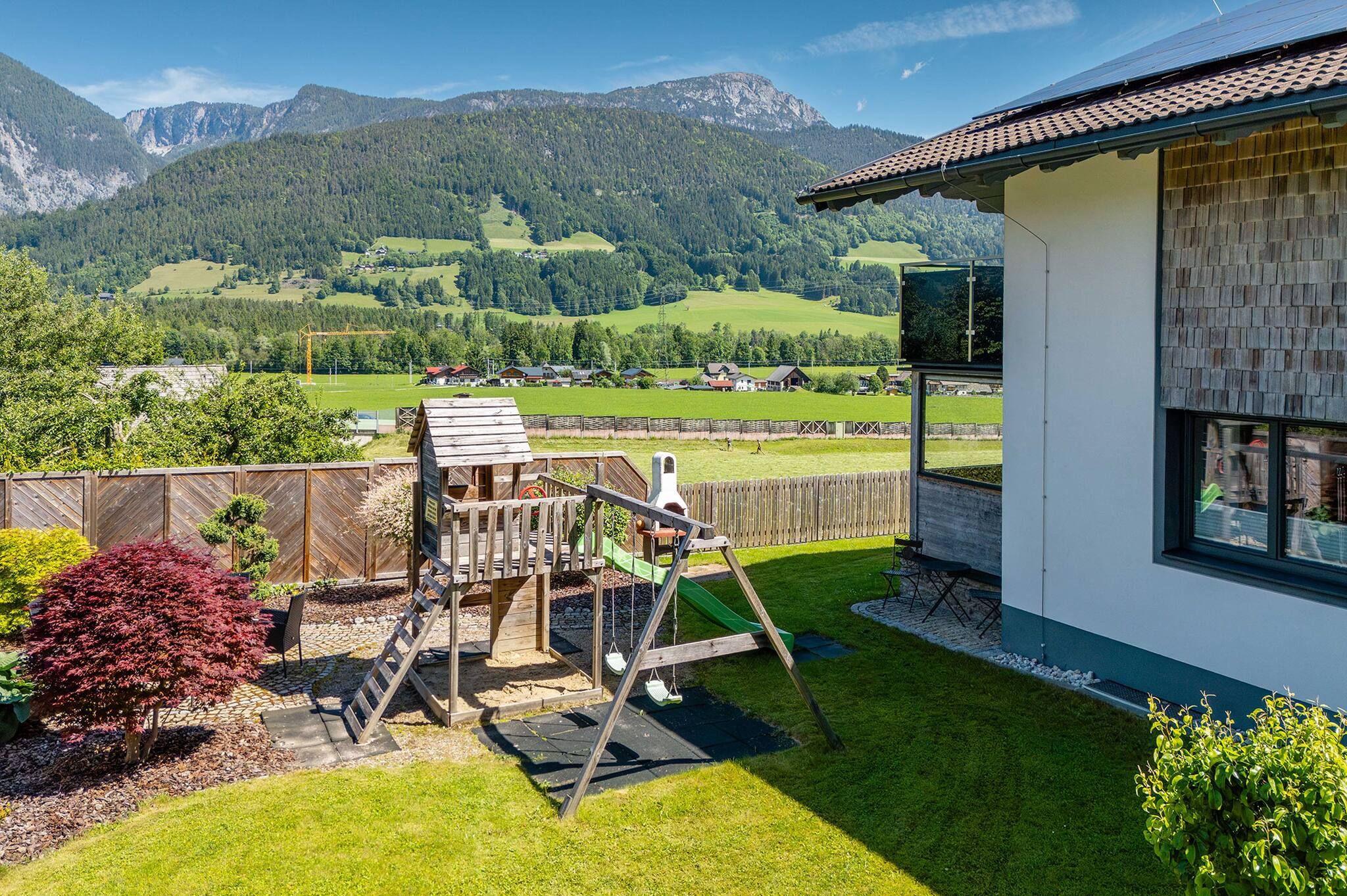A residential property with a wooden play structure, a well-maintained lawn, and a view of a mountainous landscape.