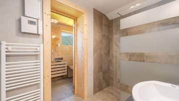 Ein modernes Badezimmer mit einer großzügigen Badewanne, einer Duschkabine und einer Holztür zum Sauna-Bereich.