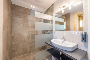 Ein modernes Badezimmer mit großem Spiegel, Waschbecken und Duschbereich.