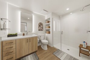 A modern bathroom with a wooden vanity, a toilet, a shower, and a mirror. - Brand-New 2BR/2BA Home, Pool View, Sleeps 6! (Lake Forest)