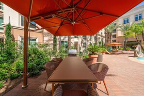 An outdoor patio with a table and chairs, surrounded by plants and a pool area. - Brand-New 2BR/2BA Home, Pool View, Sleeps 6! (Lake Forest)
