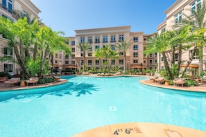 A swimming pool surrounded by lounge chairs and palm trees, with a building in the background. - Brand-New 2BR/2BA Home, Pool View, Sleeps 6! (Lake Forest)