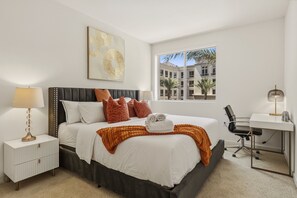 A hotel room with a bed, bedside table, lamp, and a desk with a chair. - Brand-New 2BR/2BA Home, Pool View, Sleeps 6! (Lake Forest)