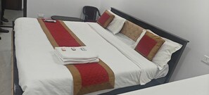 Una cama bien hecha con una colcha marrón y roja, una toalla blanca doblada y un teléfono inteligente sobre la cama.