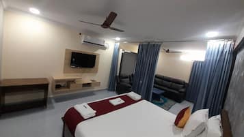 Hotellihuone, jossa on sänky, työpöytä, televisio, sohva ja kattotuuletin.