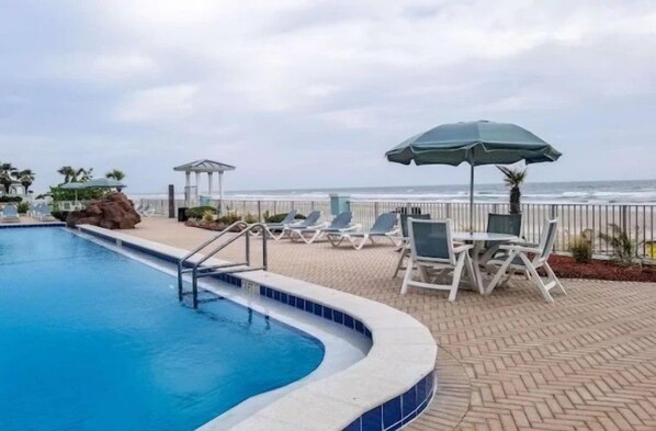 Una piscina amb gandules i ombrel·les, un porxo i vista a l'oceà.