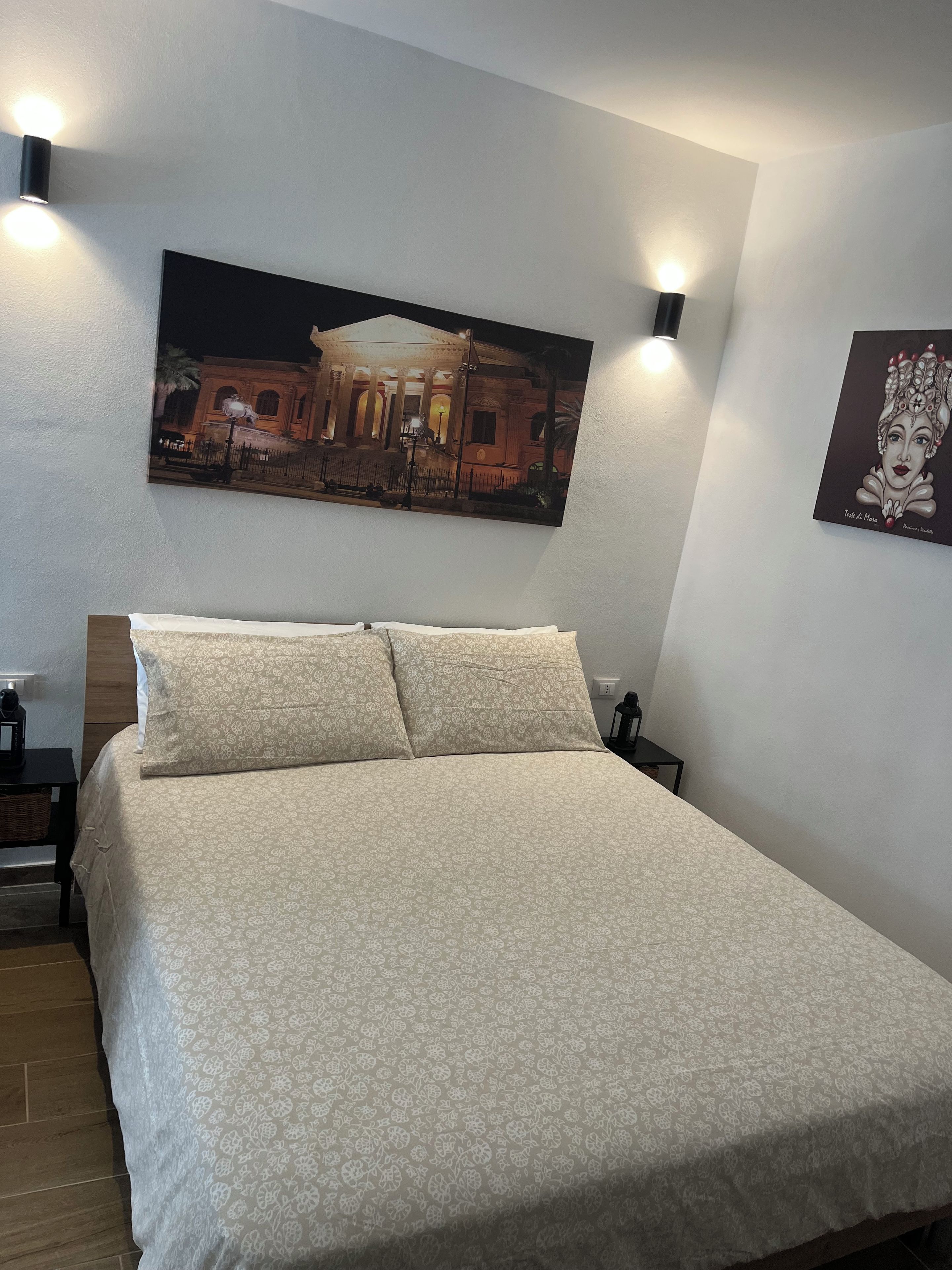 A neatly made bed with a patterned bedspread, a nightstand with a lamp, and two wall-mounted light fixtures.