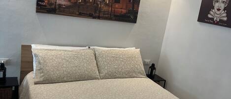 A neatly made bed with a patterned bedspread, a nightstand with a lamp, and two wall-mounted light fixtures.