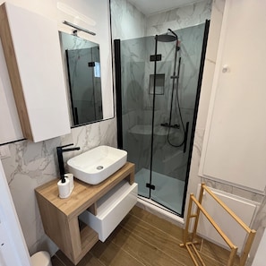 Ein modernes Badezimmer mit einer gläsernen Dusche, einem weißen Waschbecken und einer Holz-Waschplatzbank.