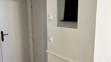 Un couloir avec une porte blanche, une petite fenêtre en arc de cercle et un luminaire fixé au mur.