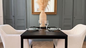 Une table à manger avec deux chaises, un vase contenant de l’herbe des pampas et un miroir encadré accroché au mur.