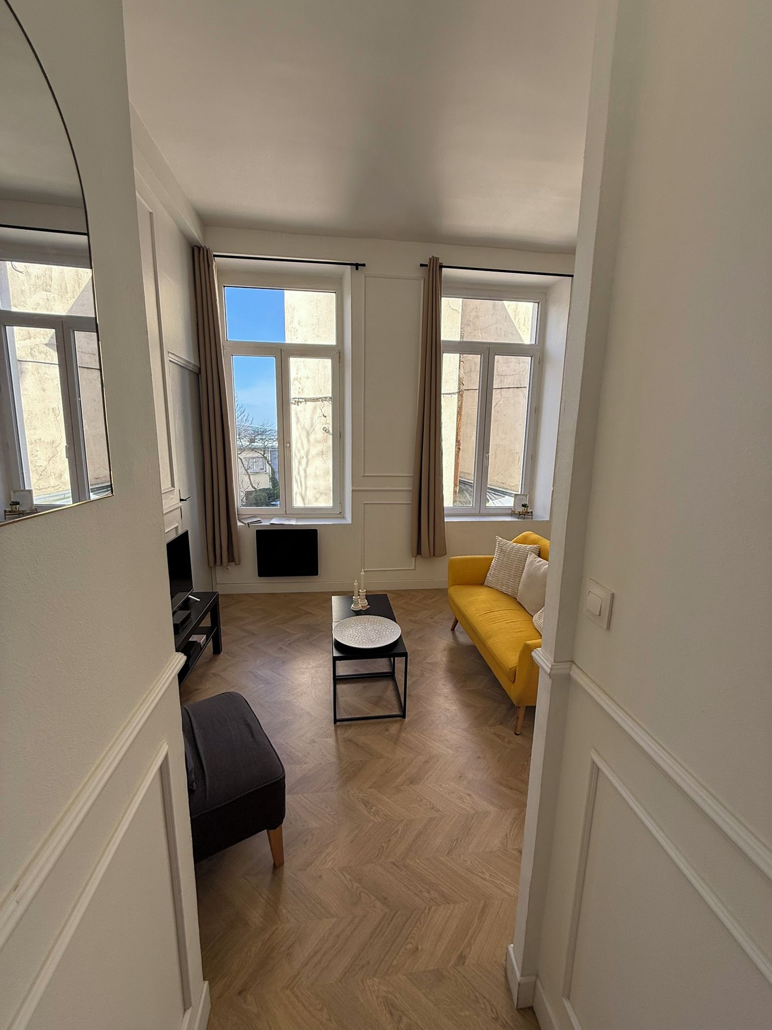 Une pièce avec un canapé jaune, une petite table et une fenêtre avec des rideaux.