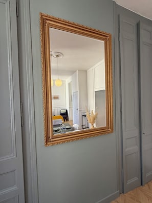 Ein Zimmer mit einem großen, verzierten Spiegel an der Wand, einer Tür und einem Blick auf einen Essbereich mit einem gelben Stuhl und einem Tisch.