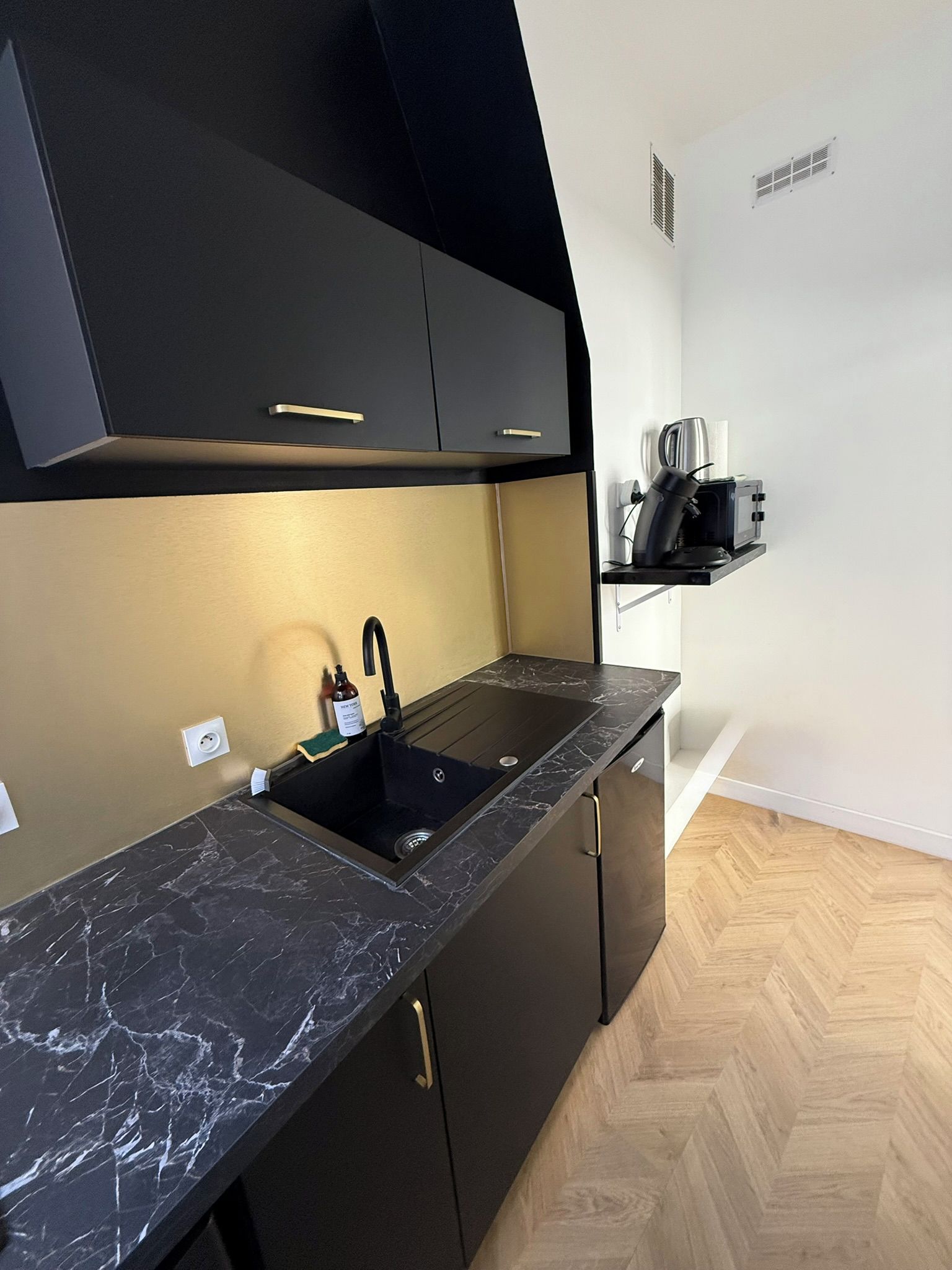 Una cocina moderna con encimera negra, un fregadero y un microondas sobre una estantería.