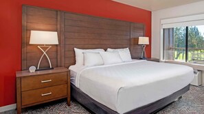 Habitación de hotel con una cama grande, dos mesitas de noche con lámparas, una pared de acento roja y un ventanal con vistas.