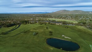 Vue aérienne d’un terrain de golf avec un étang, des arbres et une montagne en arrière-plan.