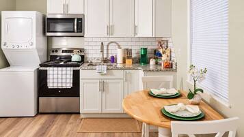 A compact kitchen with white cabinets, a microwave, a stove, and a sink. There's a dining area with a table and chairs.