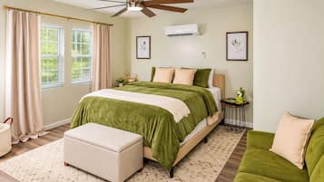 A bedroom with a bed, a ceiling fan, an air conditioning unit, a bedside table, a nightstand, a window with curtains, and a green couch.