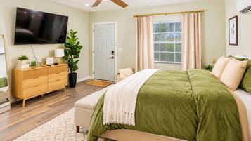 A bedroom with a bed, a TV, a dresser, and a plant.