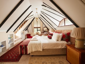 A bedroom with a sloped ceiling, a bed, bedside tables, a lamp, and a window.