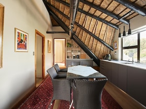 A dining area with a high ceiling, a thatched roof, and a view of a kitchen and dining room through an open door. - Shire Lodge (Cape Town)