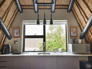 A kitchen with a large window, a sink, a kettle, a microwave, and hanging lights. - Shire Lodge (Cape Town)