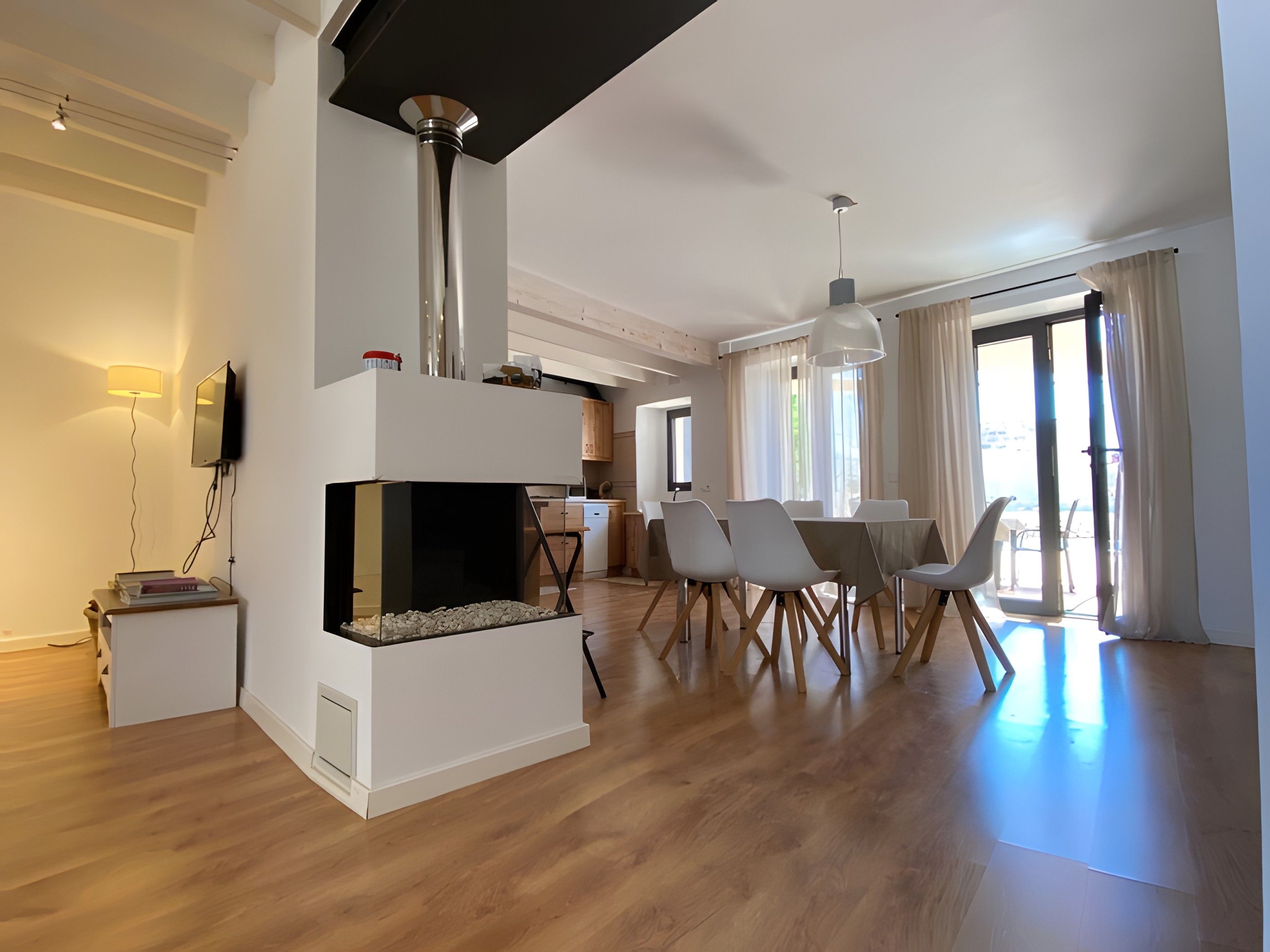 Un salon moderne avec une cheminée, un coin repas et une cuisine en arrière-plan.